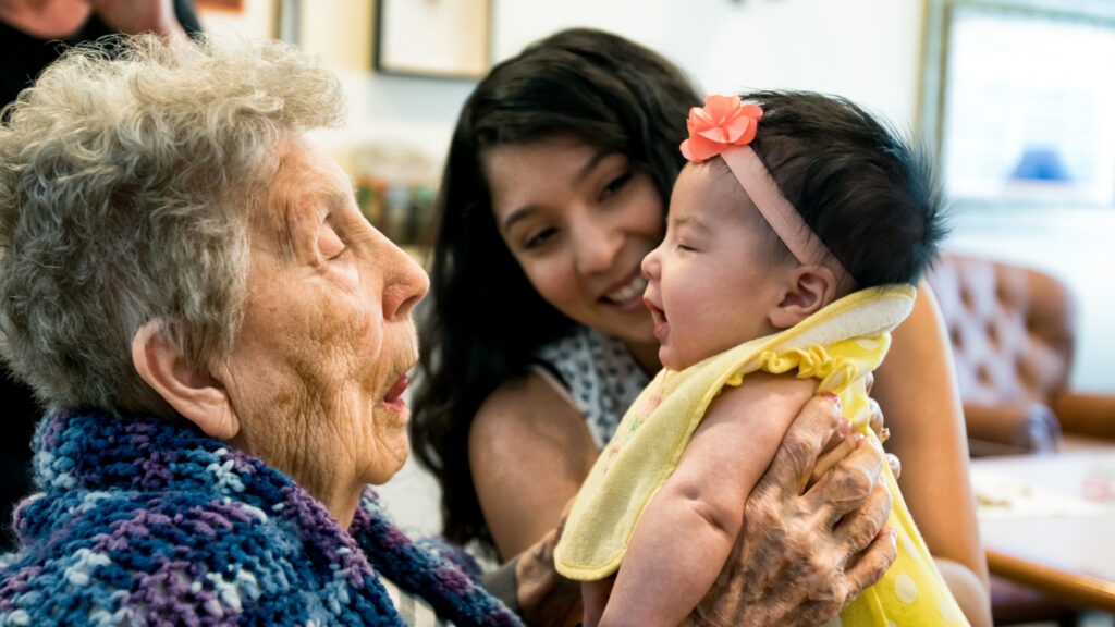 Older woman, baby, and mother smiling together.